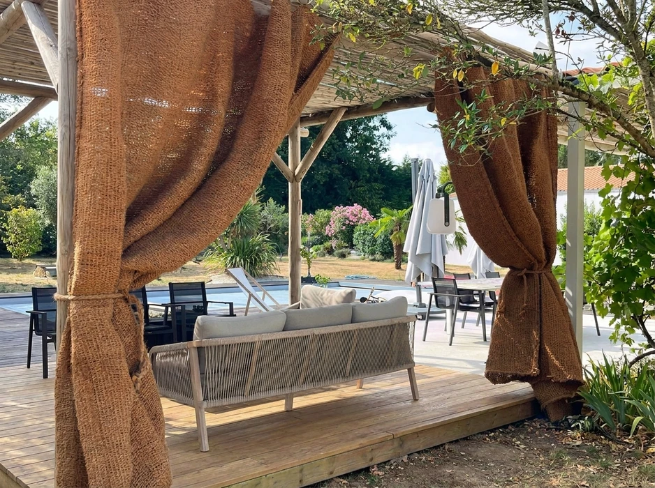 Terrasse extérieure avec pergola en bois naturel ornée de rideaux en toile de jute ocre nouée