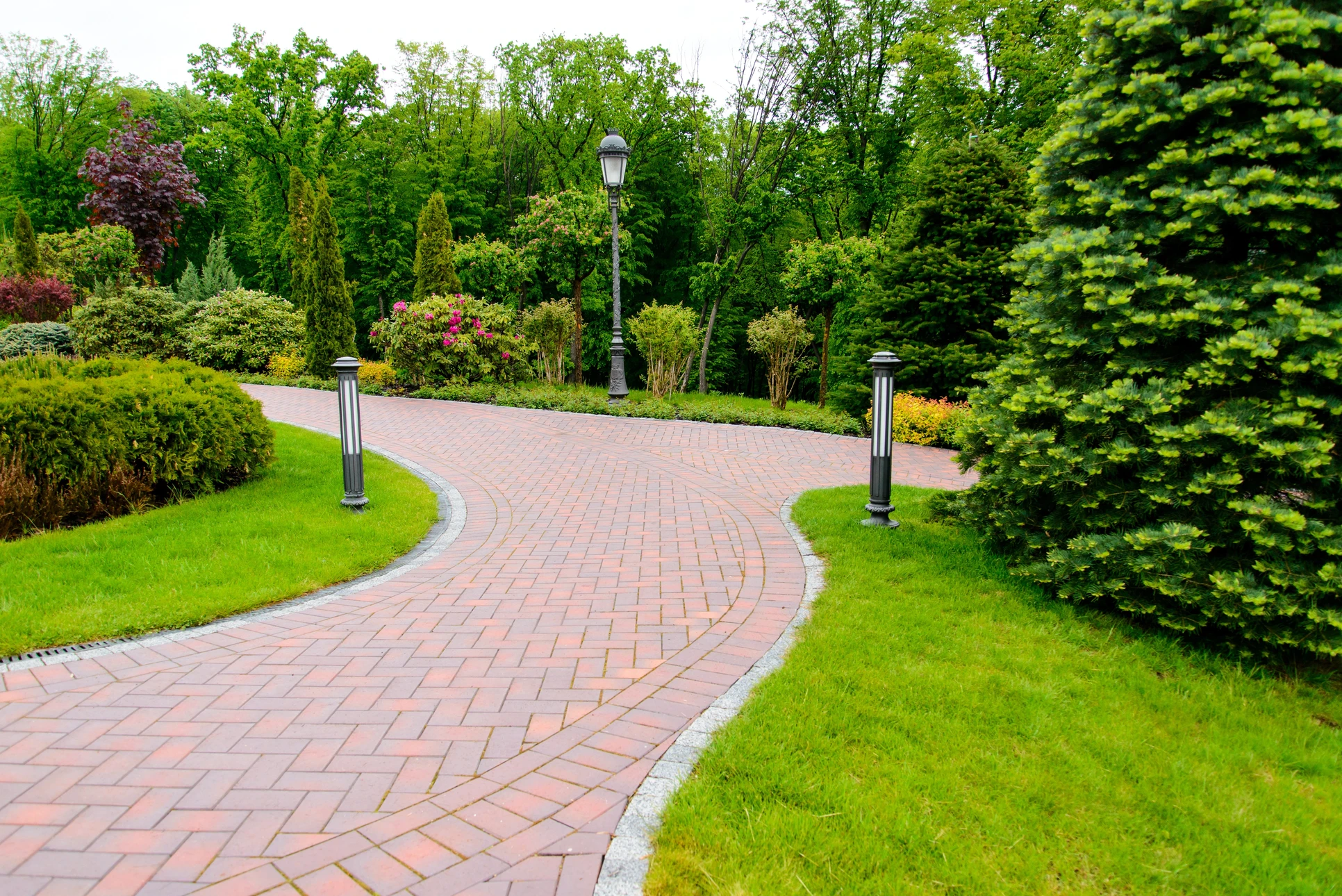 Aménagement paysager extérieur avec allée courbe en briques rouges ornée de motifs décoratifs floraux en pierre naturelle