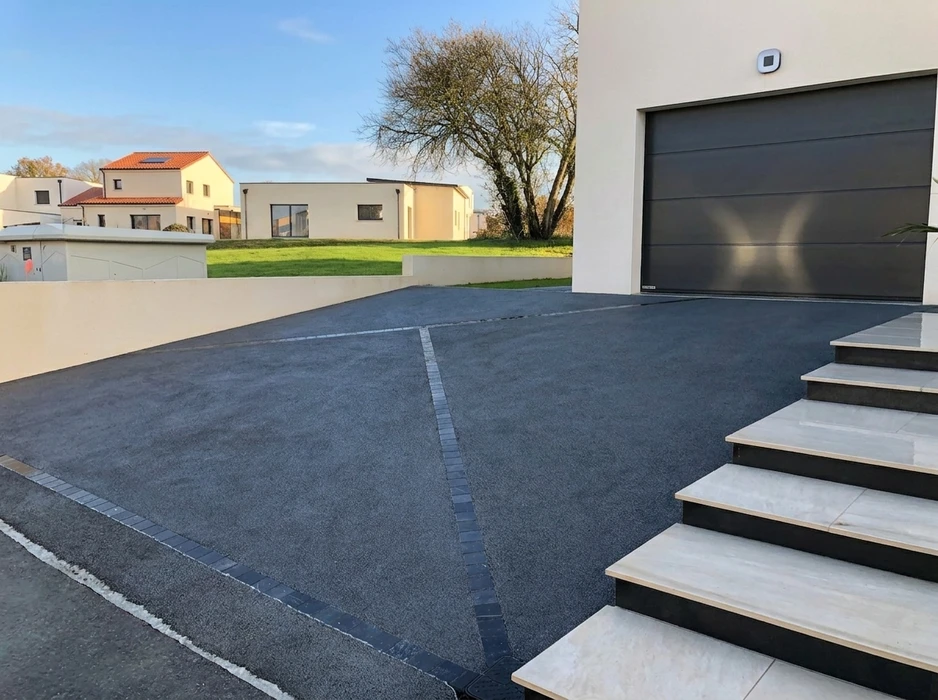 Allée de maison moderne avec revêtement en enrobé bitumineux gris anthracite, délimité par des pavés autobloquants en granit formant joints décoratifs en croix