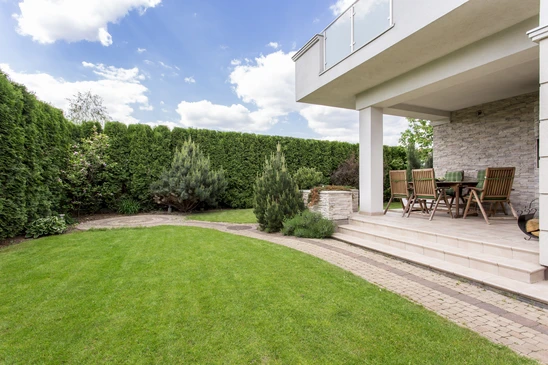 Jardin résidentiel moderne avec terrasse couverte aménagée, salon de jardin en teck, pelouse entretenue et haies taillées