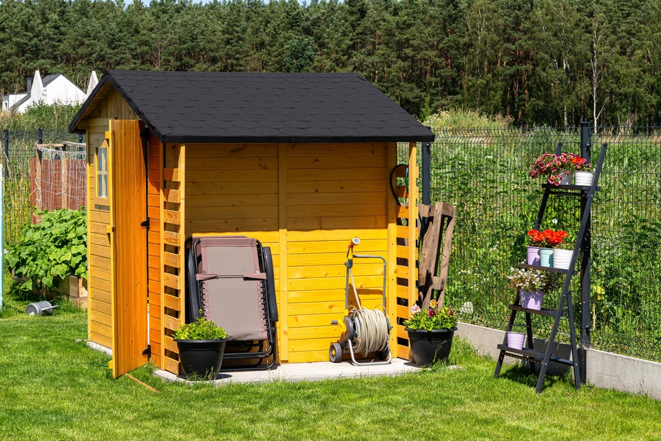 Jardin résidentiel aménagé avec abri de rangement en bois, récupérateur d'eau de pluie vert, outils de jardinage et plantes grimpantes